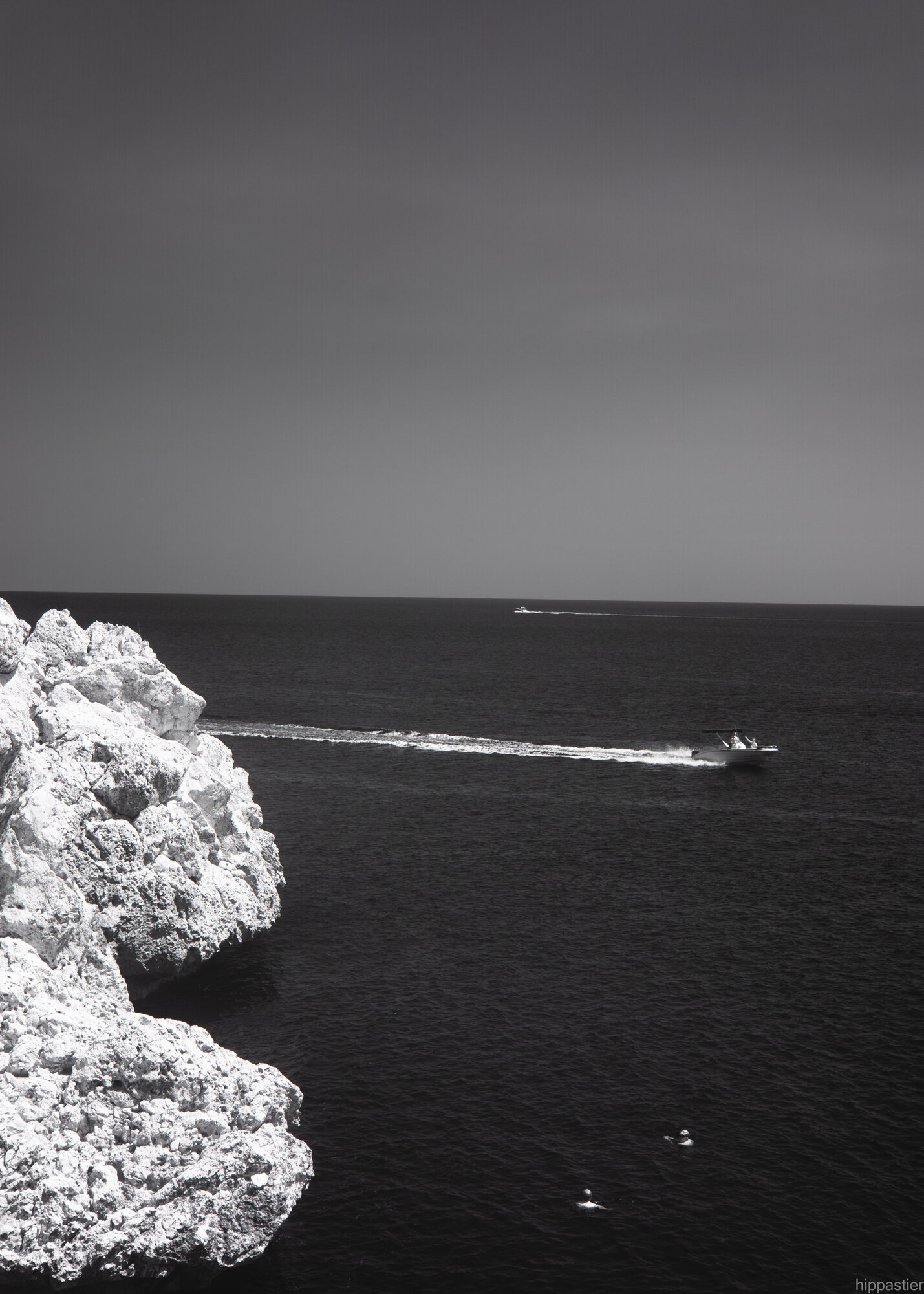 White rocky cliff over dark sea with a distant boat, black and white infrared, Cyprus
